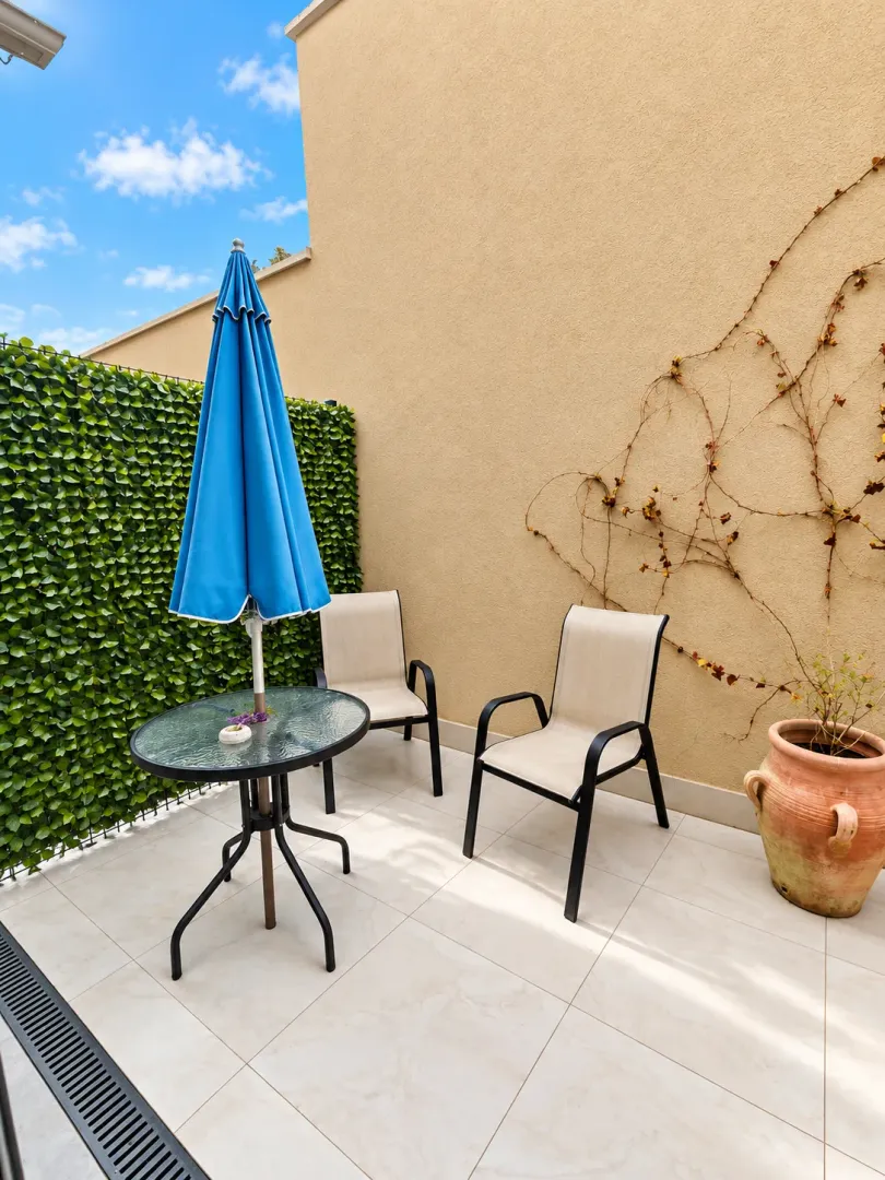 Small terrace with a table, chairs, parasol, and decorative pots.