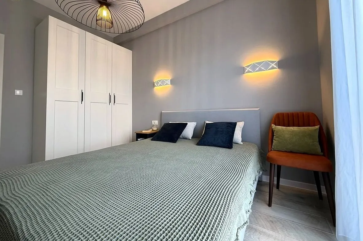 Moderna spavaća soba sa bračnim krevetom, bijelim garderoberom i zidnim lampama.