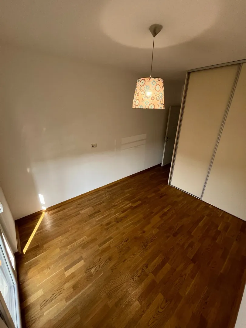 Prazna prostorija sa drvenim podom, ugradnim plakarom i visećom lampom.