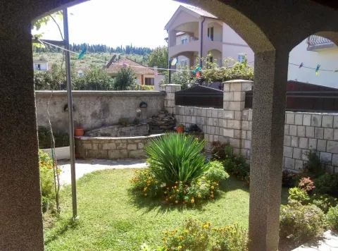 Pogled iz natkrivenog trijema na uređeno dvorište sa zelenilom i okolne kuće. - image 4