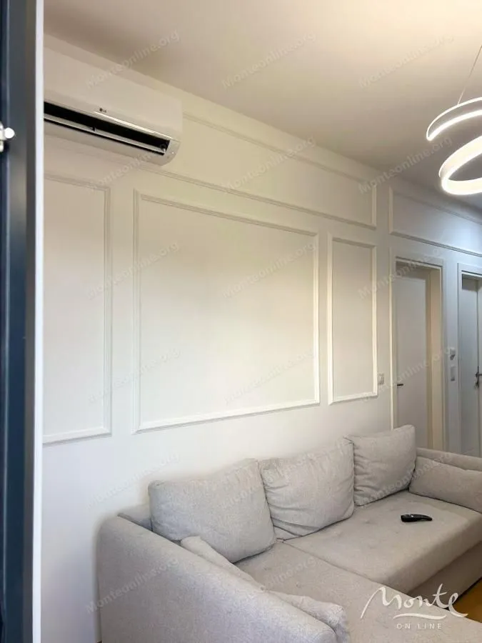 Dnevna soba sa udobnom sivom garniturom i dekorativnim zidnim lajsnama.