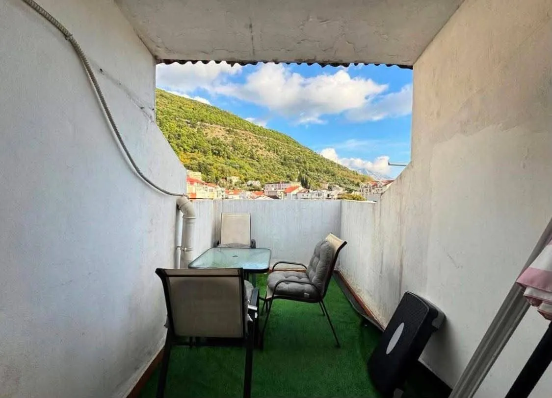 Manji namješten balkon sa stolom, stolicama i pogledom na brdo.