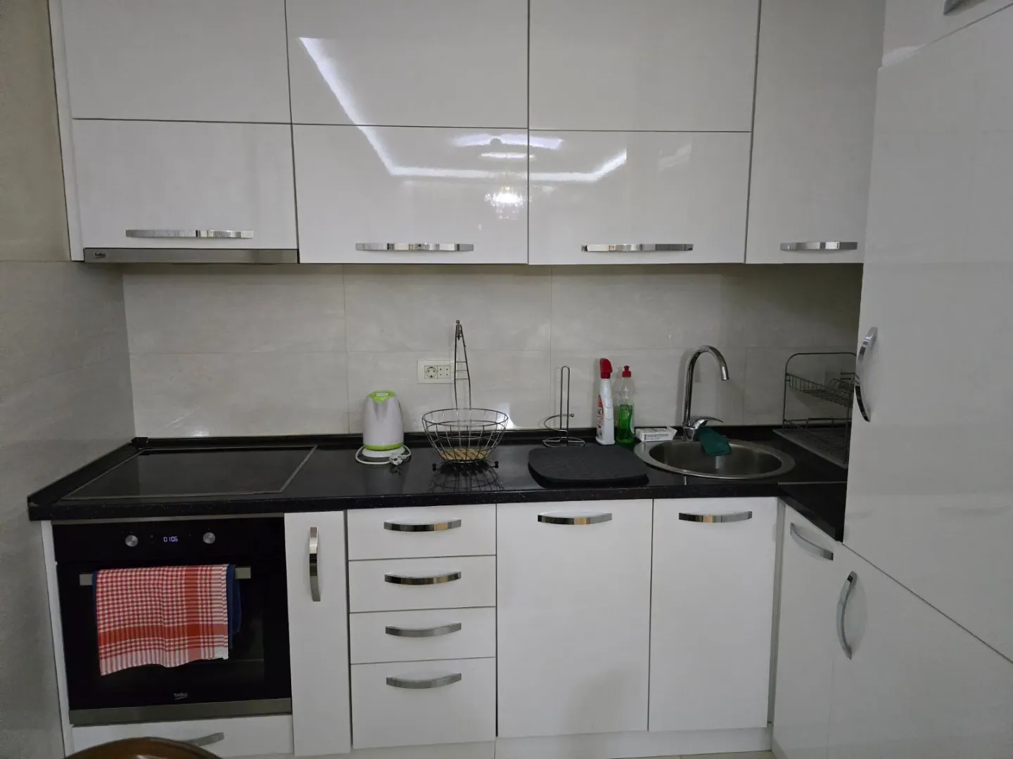 Moderna bijela kuhinja sa ugrađenom rernom, pločom i sudoperom.