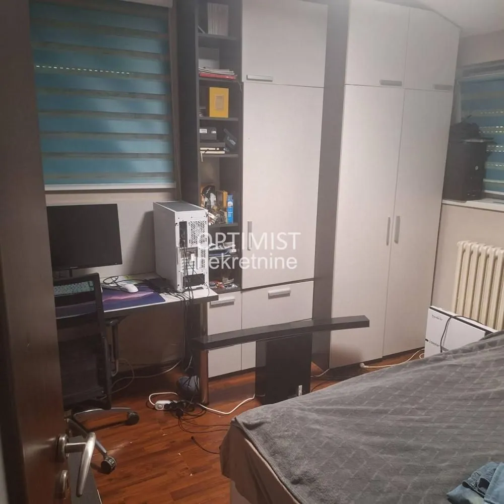 Manja spavaća soba sa krevetom, garderoberom i radnim stolom sa računarom.