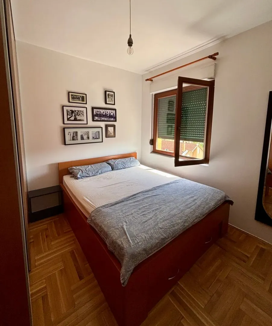 Bedroom with a double bed, wooden parquet flooring, and a window overlooking the outside.