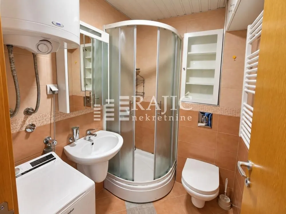 Compact bathroom with a shower cabin, sink, toilet, and water heater.