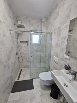Savremeno opremljeno kupatilo sa tuš kabinom, umivaonikom i toaletom u sivim tonovima. - image 5