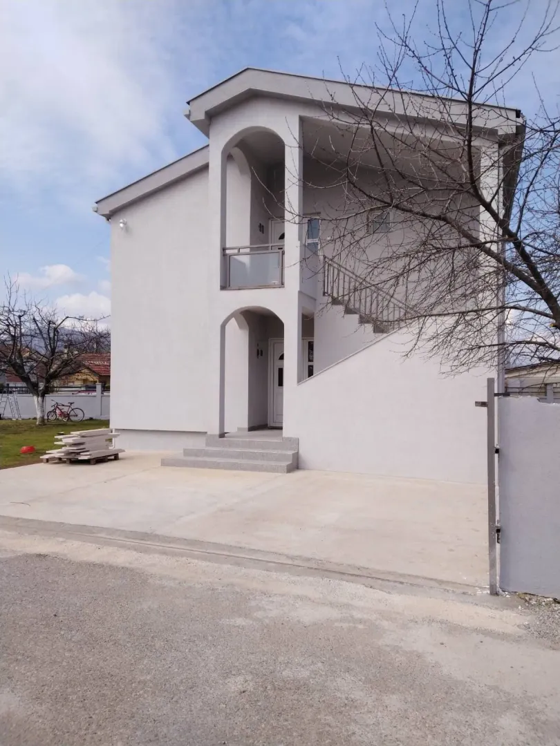 A two-story house with a light facade and a paved yard.