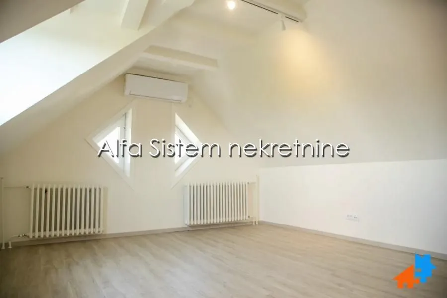 Empty attic room with light walls, wooden flooring, and radiators.
