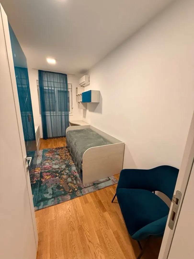 Manja spavaća soba sa krevetom, plavom foteljom i garderoberom.