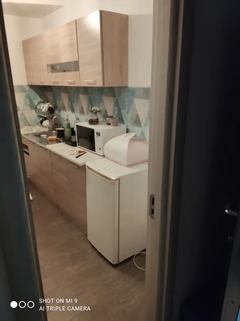 View of a small kitchen with wooden cabinets and white appliances through the doorway.