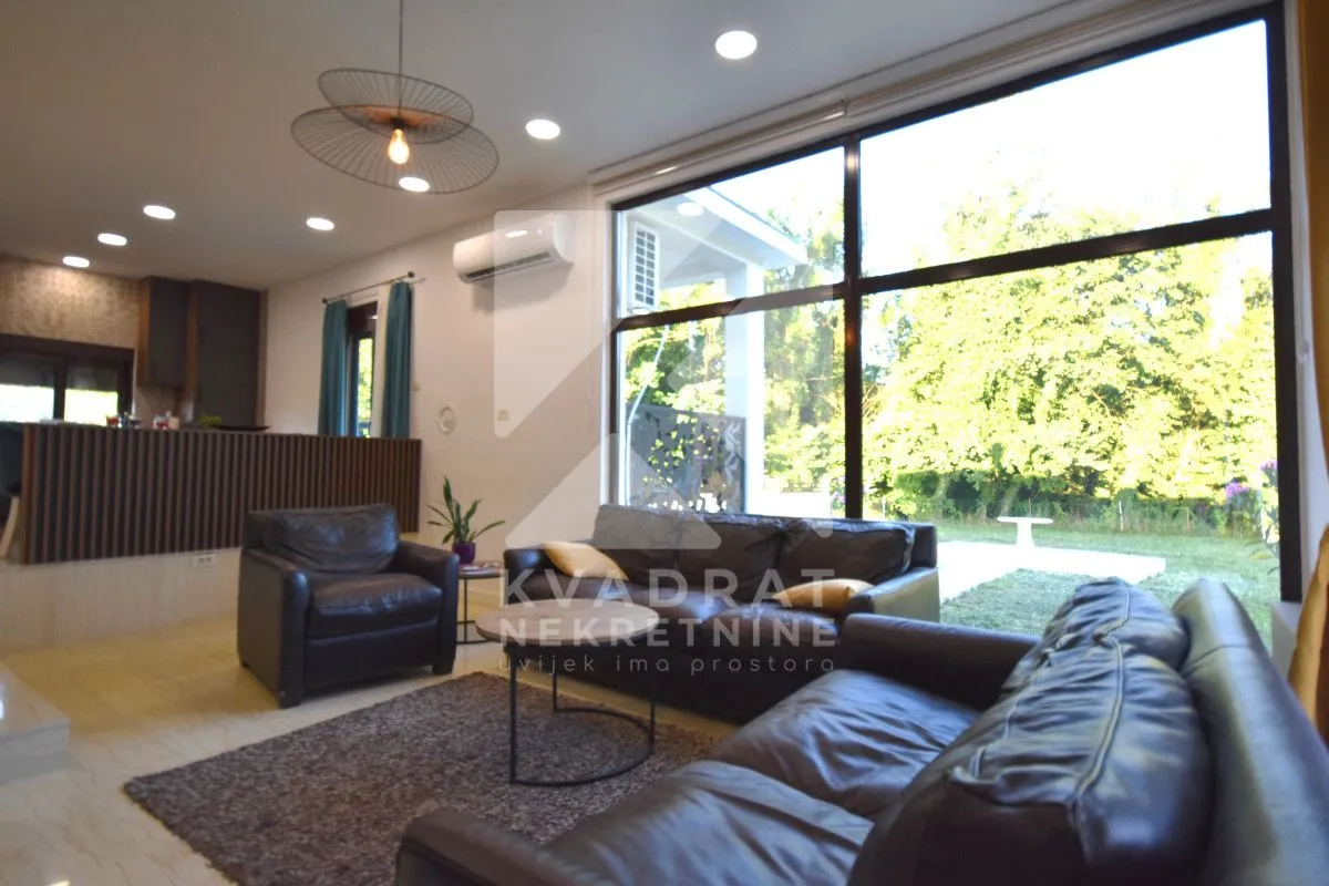 Living room with leather sofas and large glass windows overlooking the yard.