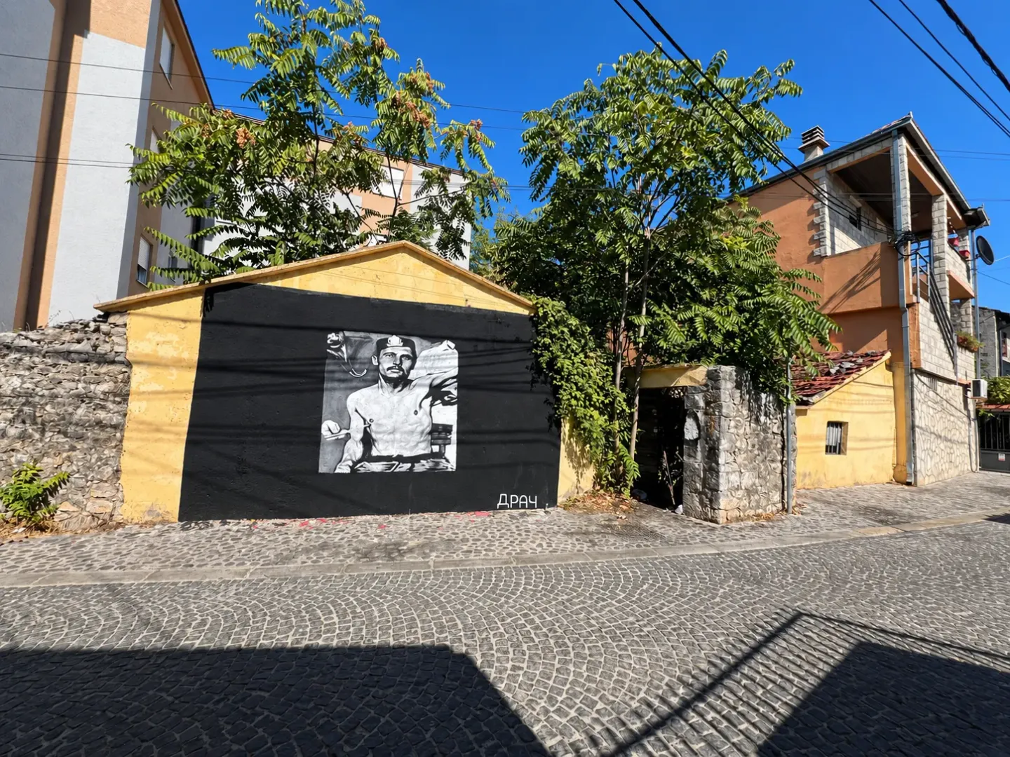 Pogled na ulicu sa kaldrmom i fasadom zgrade sa muralom.