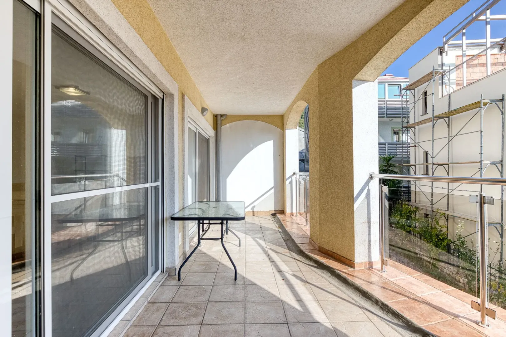 Covered balcony with ceramic tiles and glass railing.