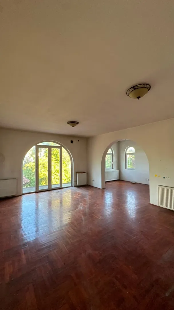 Empty spacious room with parquet flooring and arched windows.