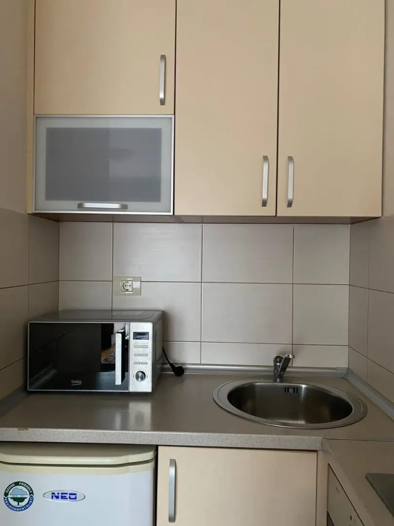 Mala funkcionalna kuhinja sa sudoperom, mikrotalasnom pećnicom i kuhinjskim elementima.