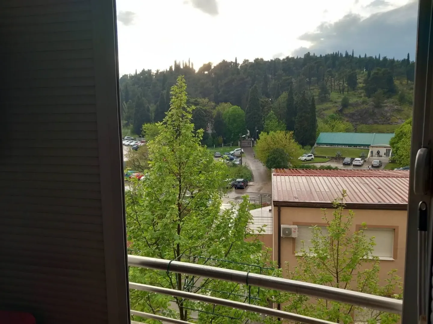 Pogled sa prozora na okolno zelenilo i brdo u daljini.