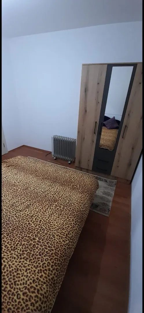 Jednostavna spavaća soba sa krevetom, drvenim ormarom i radijatorom.