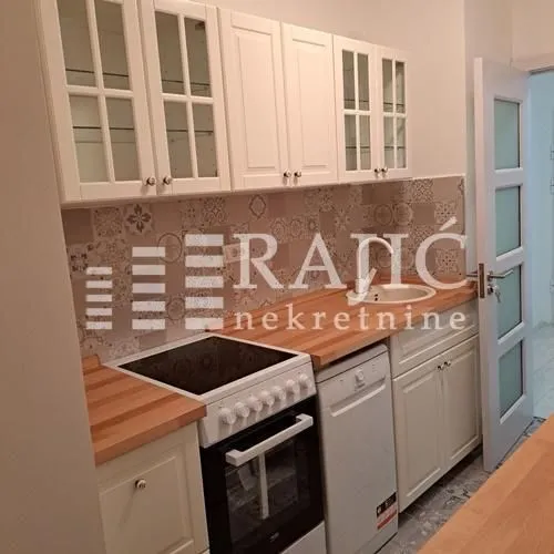 Compact equipped kitchen with white cabinets and a wooden countertop.