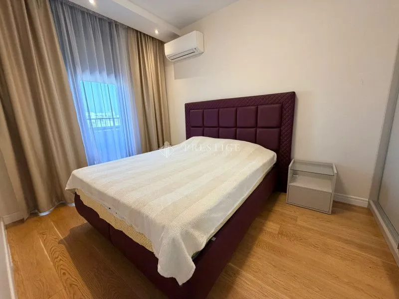 Uređena spavaća soba sa bračnim krevetom, noćnim ormarićem i klima uređajem.