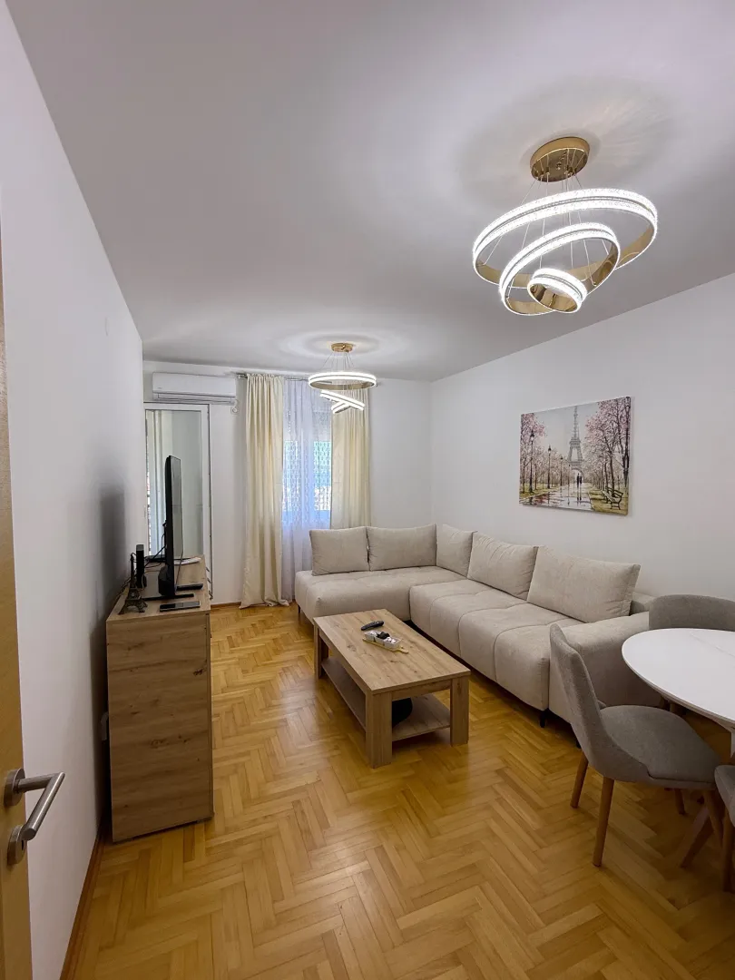 Living room with a sectional sofa, wooden parquet flooring, and modern chandeliers.