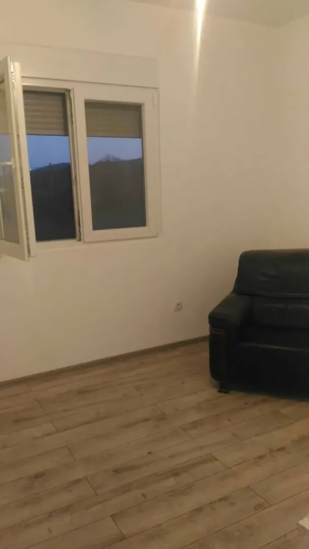 A simple room with light walls, wooden flooring, and a black leather armchair next to the window.