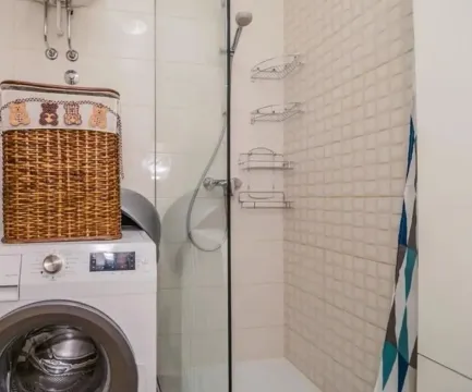 Bathroom with a shower cabin, washing machine, and woven laundry basket. - image 6