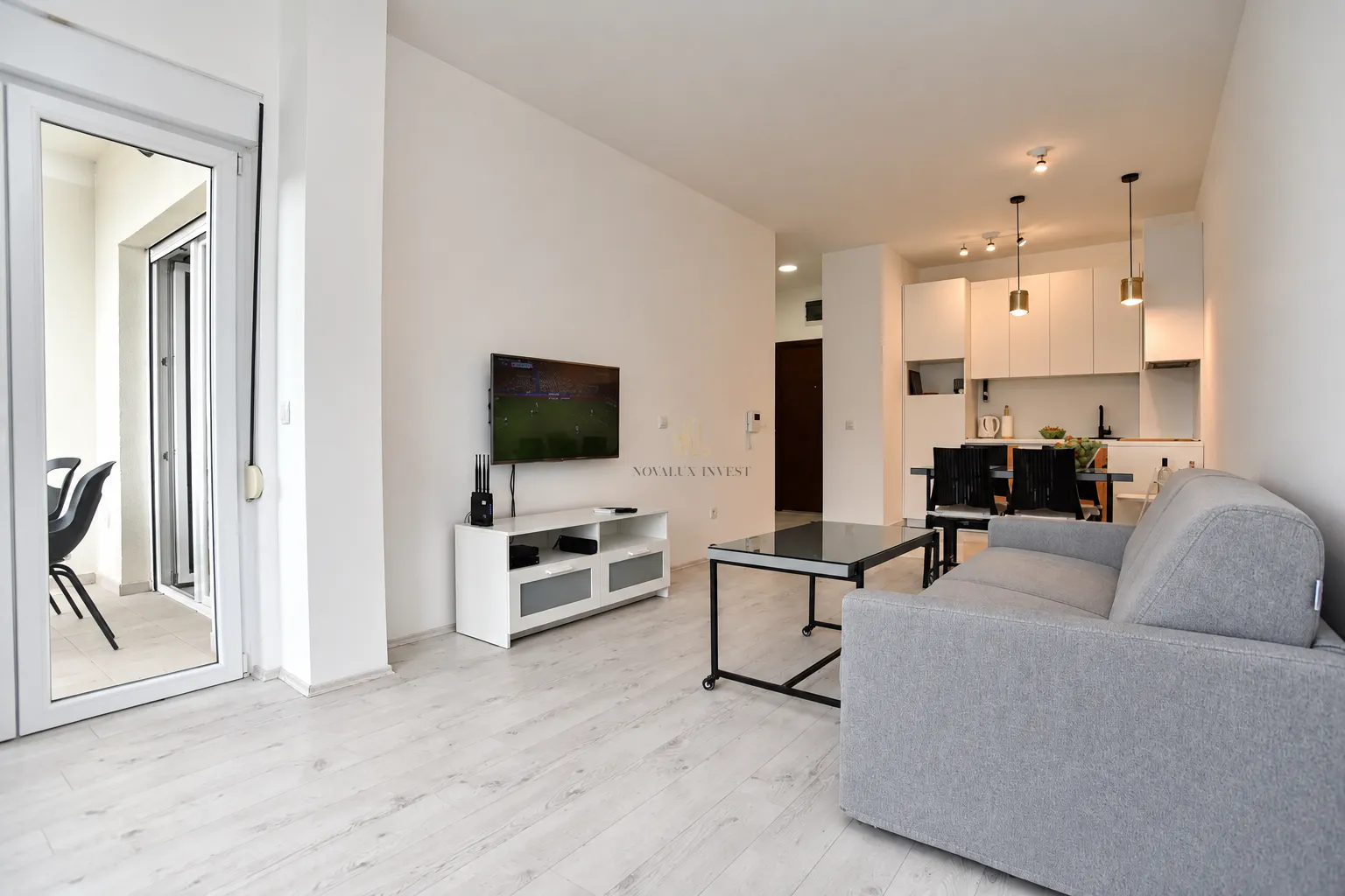 Living room with sofa, television, and kitchen in the background.