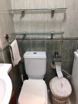 Bathroom with a toilet, ceramic tiles, and glass shelves. - image 8