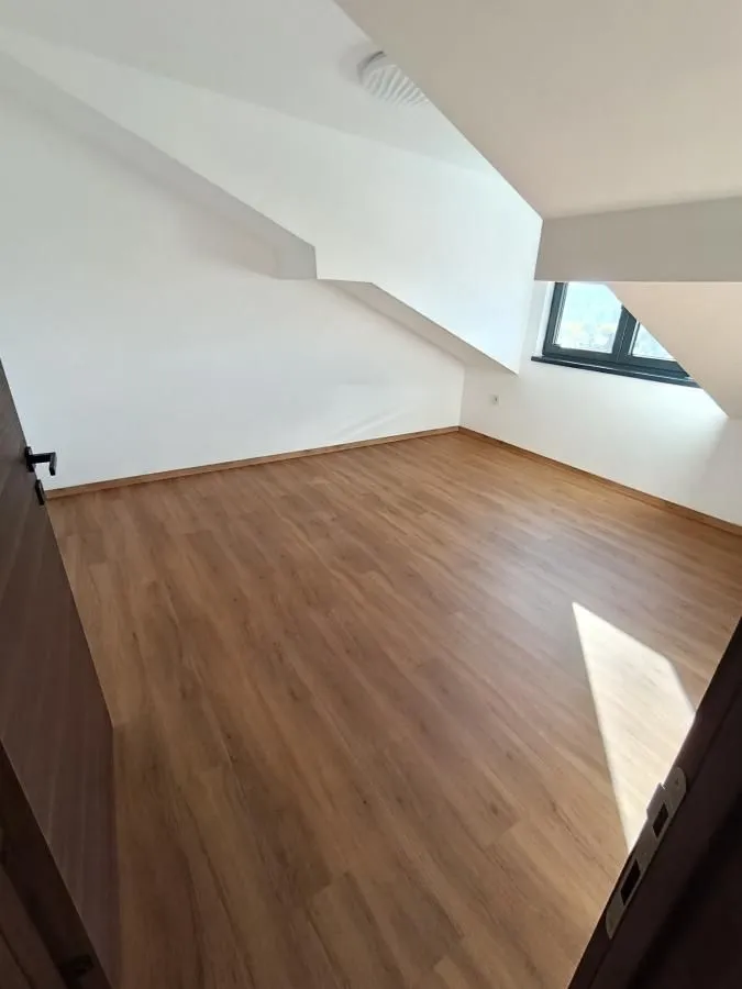 Prazna soba sa laminatom i kosim plafonom.