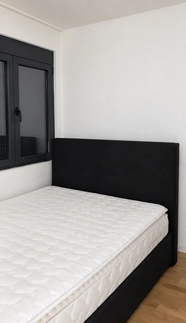 Spavaća soba sa bračnim krevetom i tamnim okvirom prozora.