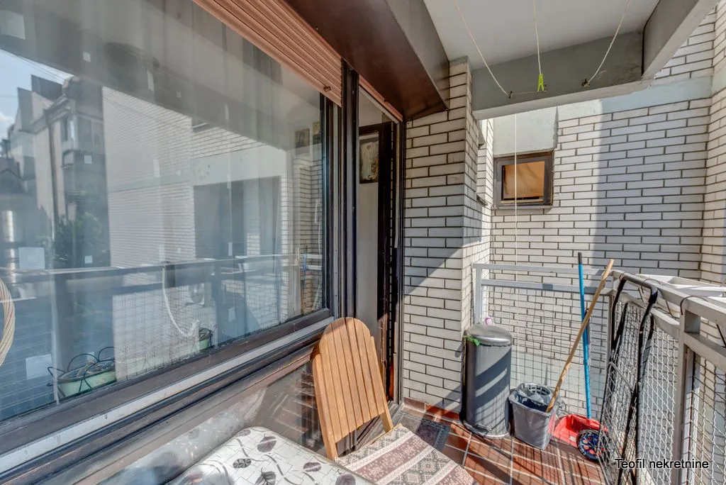 Small covered balcony with a table, chair, and cleaning supplies.