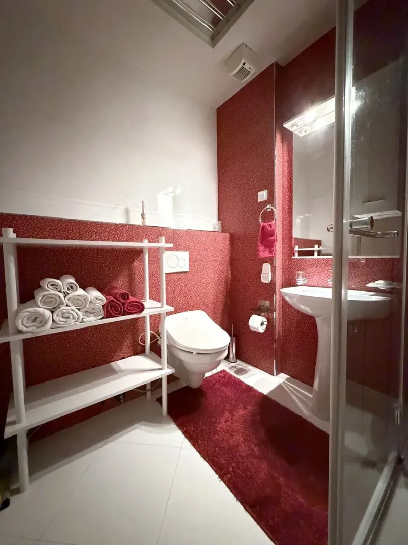 Modern bathroom with a toilet, washbasin, shower cabin, and towel shelf.