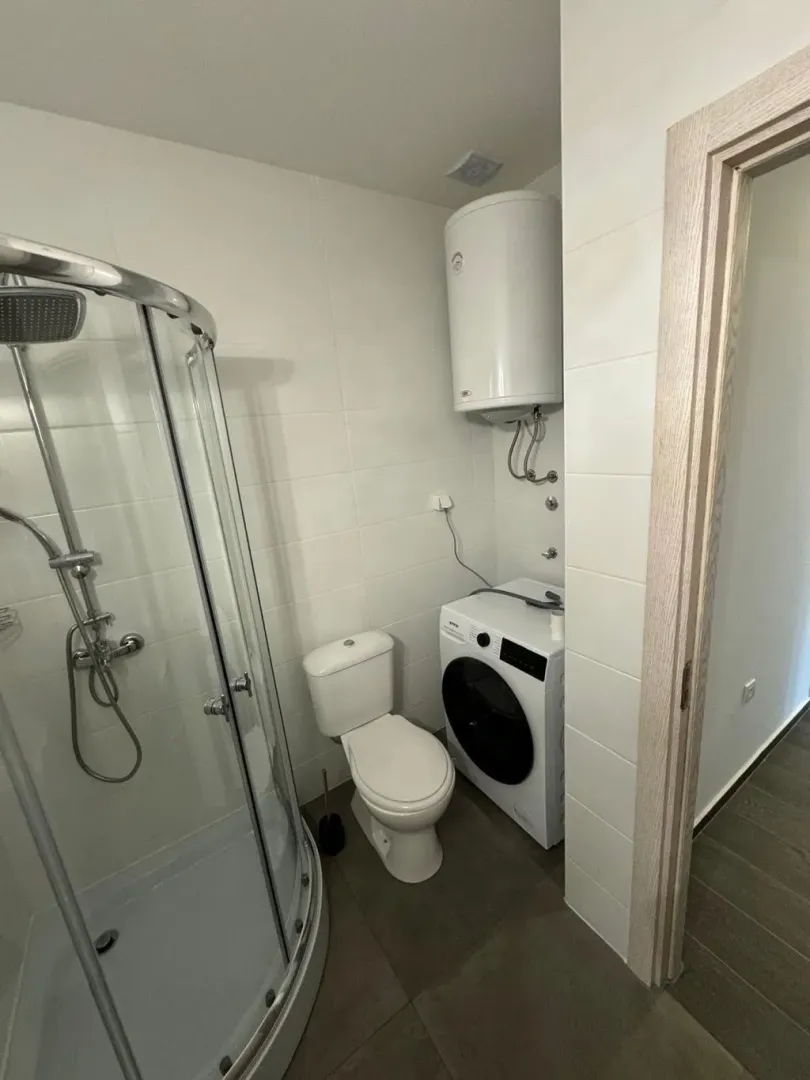 Smaller bathroom with a shower cabin, toilet, and washing machine.