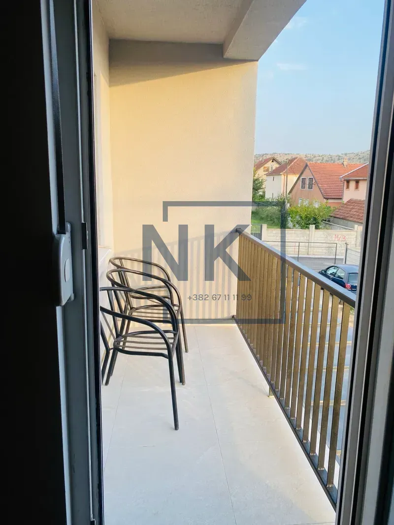 Manji balkon sa stolicama i ogradom sa pogledom na naselje.