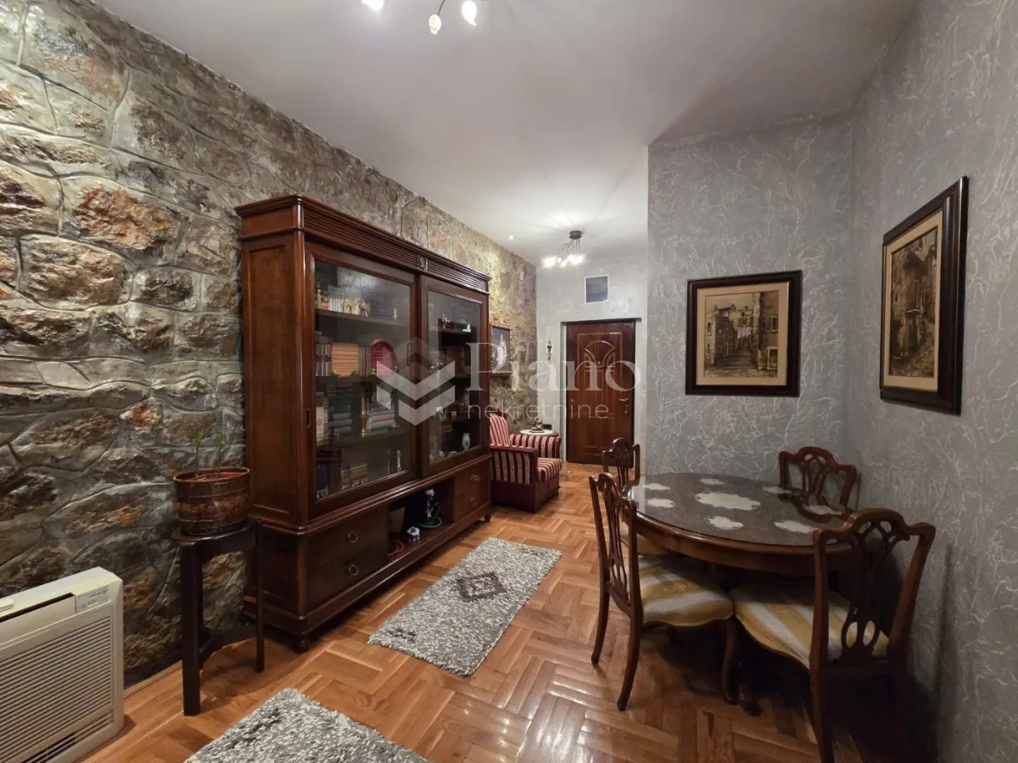 Living room with a dining table, a large wooden display cabinet, and a stone-clad wall.