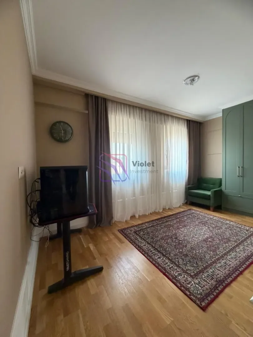 Dnevna soba sa drvenim podom, tepihom i zelenom foteljom.