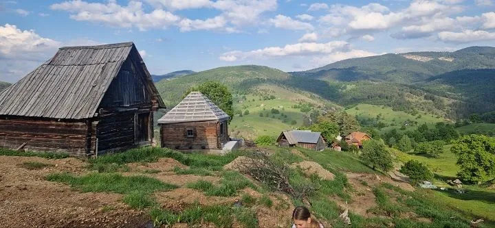 Tradicionalne drvene brvnare na bregu sa pogledom na planinu.