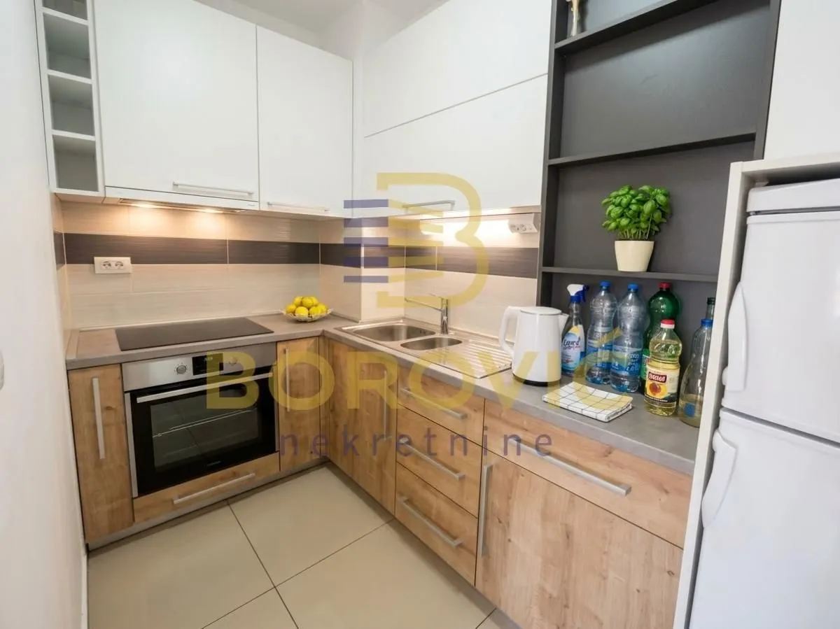 Compact kitchen with wooden lower cabinets, white wall cabinets, and a built-in oven.