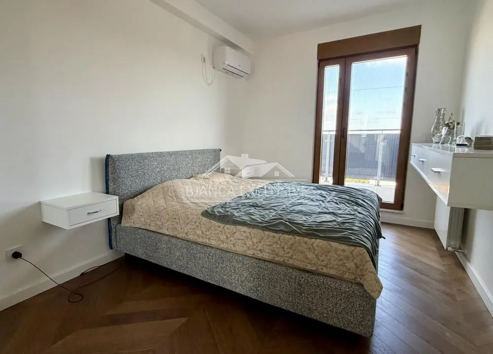 Nameštena spavaća soba sa bračnim krevetom, klima-uređajem i izlazom na terasu.