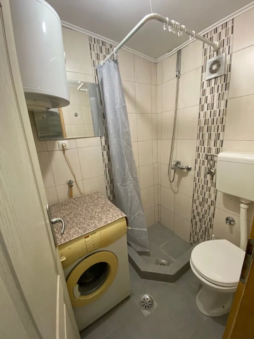 Manje kupatilo sa tuš kabinom, veš mašinom i sanitarijama.