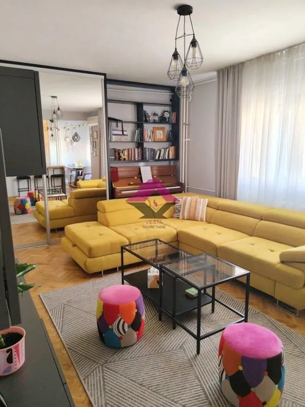 Living room with a yellow sectional sofa, coffee table, and bookshelf.