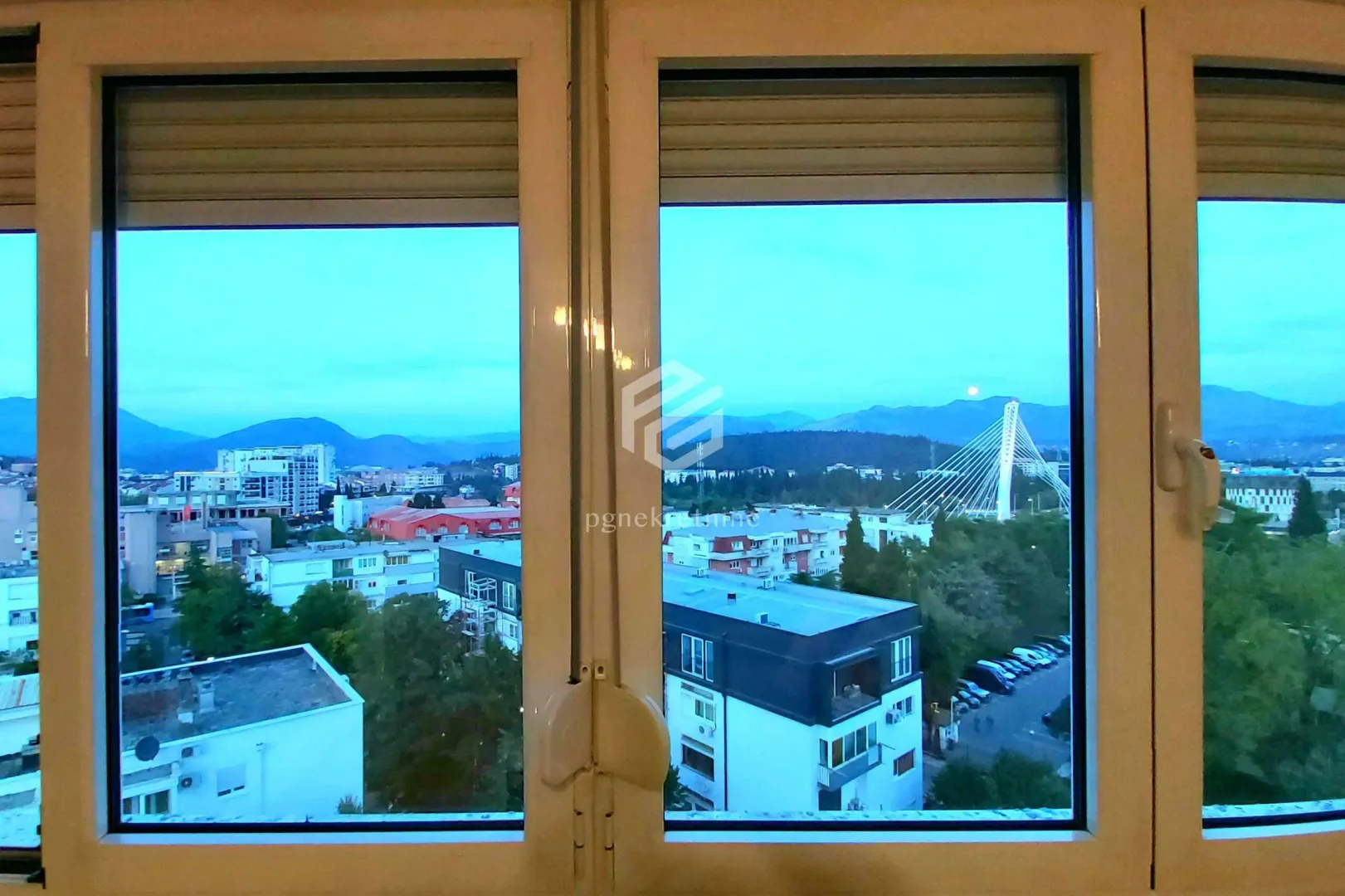 View of the city with a bridge and mountains in the background through a window.