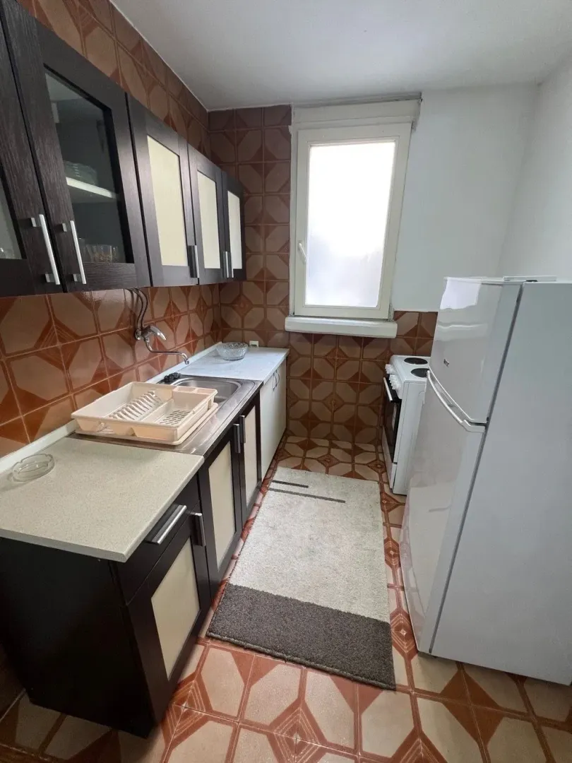 Manja kuhinja sa tamnim elementima i bijelim frižiderom.