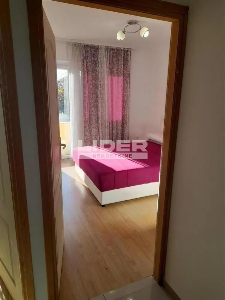 Pogled iz hodnika na nameštenu spavaću sobu sa krevetom i izlazom na terasu.