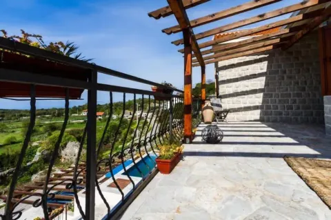 Spacious stone terrace with a wooden pergola and a view of the surrounding landscape and swimming pool. - image 7