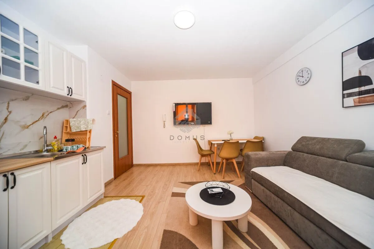 Living room with a corner sofa, dining table, and a kitchenette area.