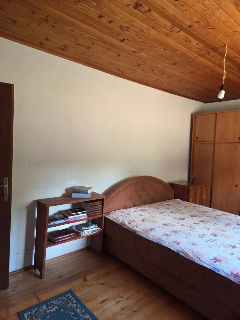 Namještena spavaća soba sa drvenim plafonom, krevetom, ormarom i policom za knjige.