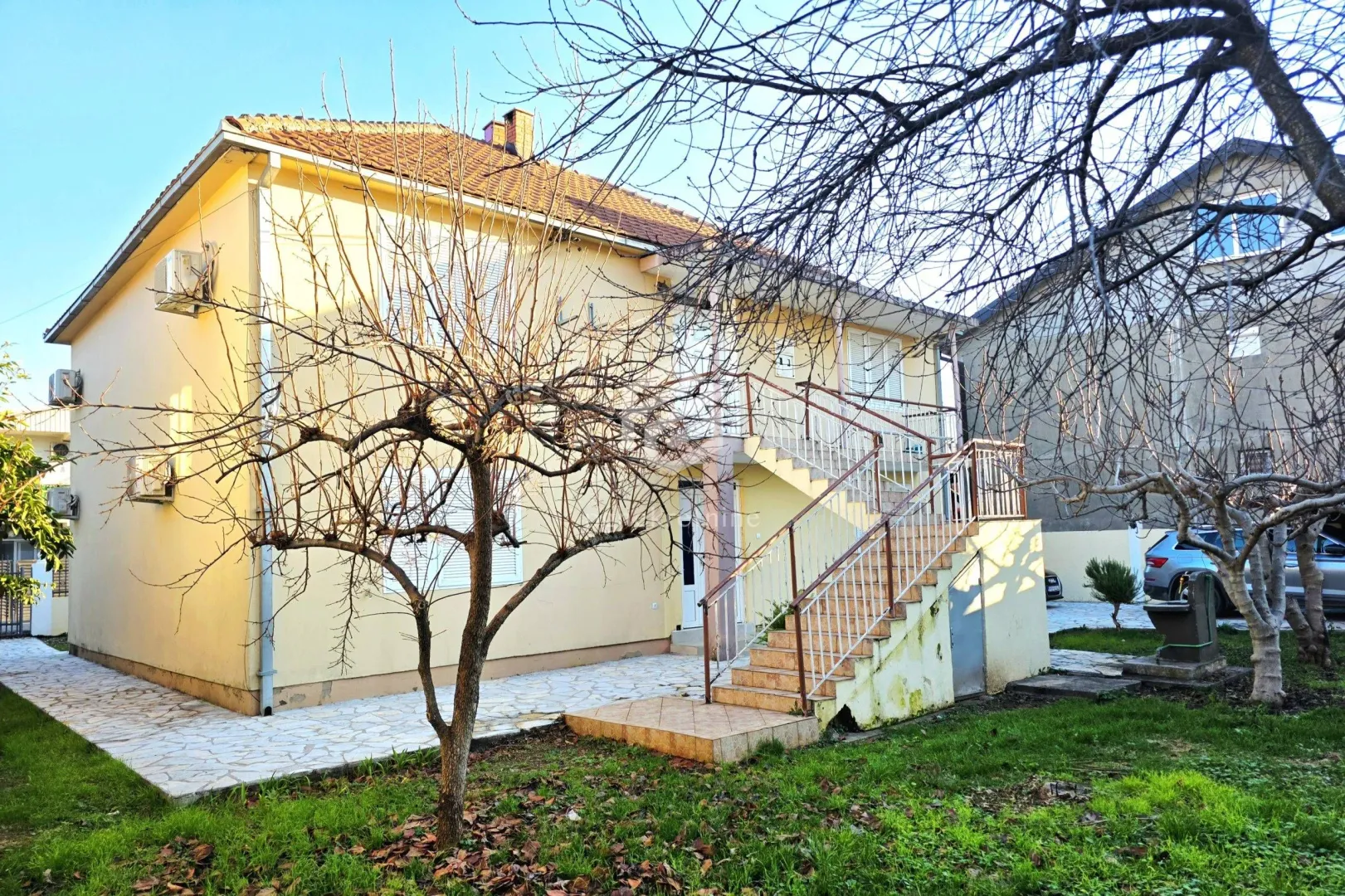 Spoljašnji izgled kuće sa dvorištem i spoljnim stepeništem.