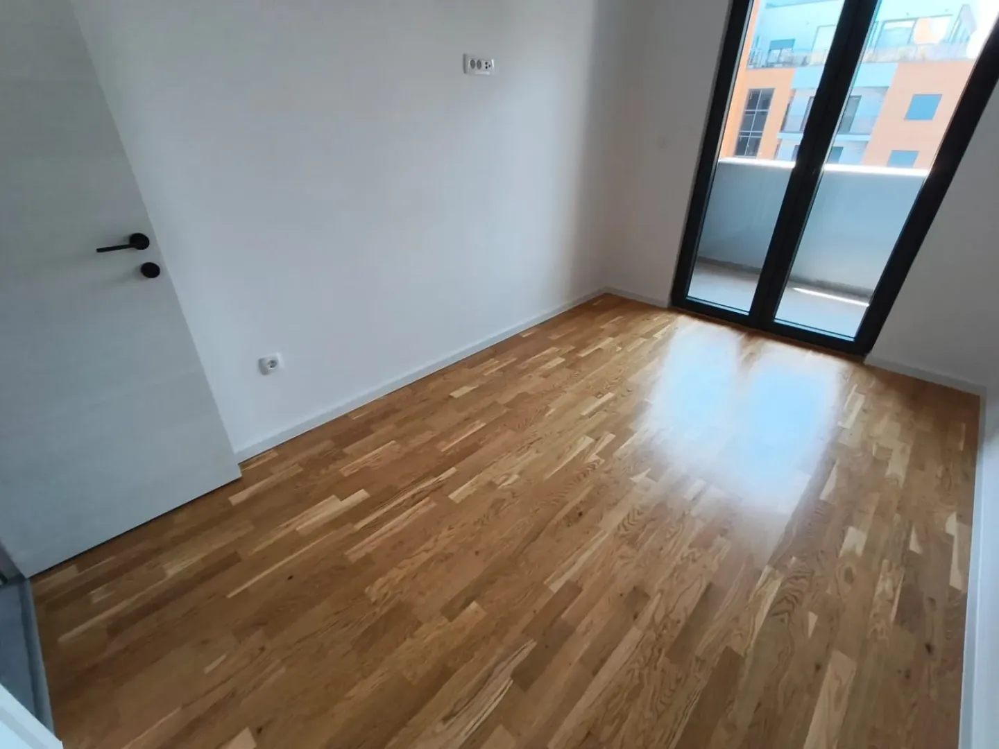 Prazna soba sa drvenim parketom i izlazom na terasu.